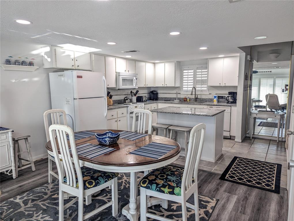 A kitchen features white cabinetry, granite countertops, a central island, and a round dining table — 815 OCEAN SHORE BOULEVARD UNIT 11A, ORMOND BEACH, FL