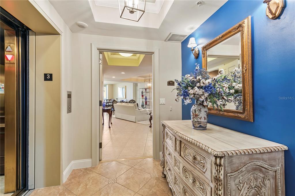 An elevator opens into a foyer with a blue accent wall, mirror, and wooden dresser — 19 AVENUE DE LA MER UNIT 305, PALM COAST, FL