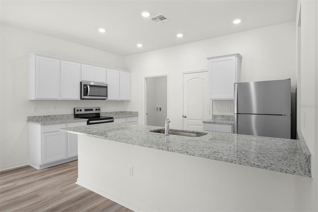 A kitchen features white cabinets, granite countertops, stainless steel appliances, and wood-look flooring — 13265 TULA LOOP, ASTATULA, FL