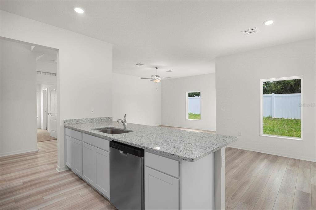 A kitchen island with a granite countertop and stainless steel sink overlooks an open living area — 13265 TULA LOOP, ASTATULA, FL