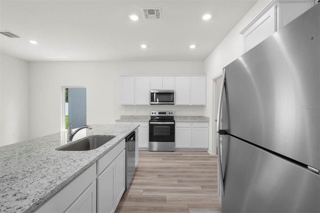 A modern kitchen features white cabinets, granite countertops, stainless steel appliances, and a center island — 13265 TULA LOOP, ASTATULA, FL