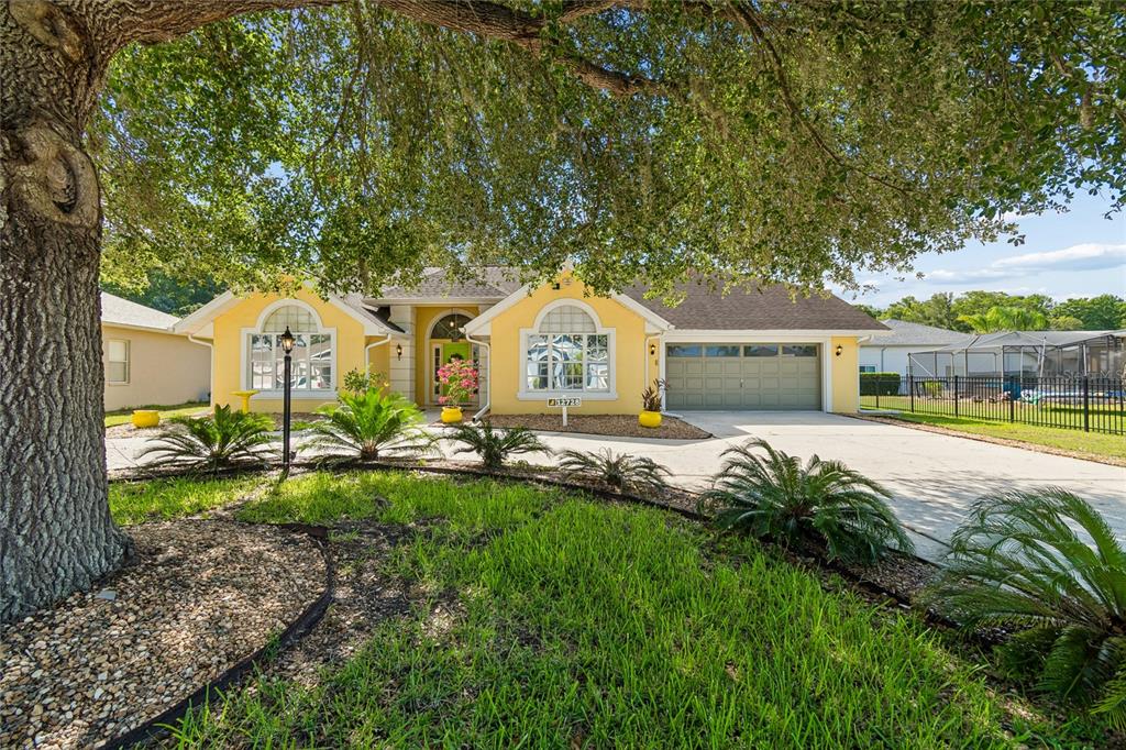 A yellow single-story house with a two-car garage and a large oak tree in front — 12728 FLAMINGO PARKWAY, SPRING HILL, FL