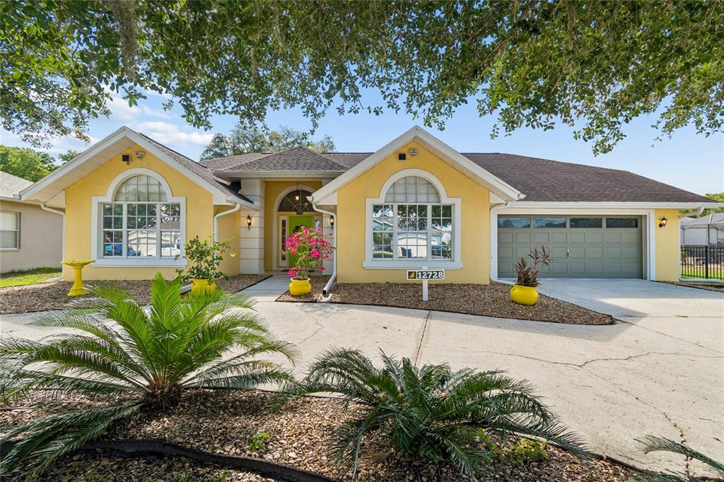 A yellow single-story house with a concrete driveway and a two-car garage — 12728 FLAMINGO PARKWAY, SPRING HILL, FL