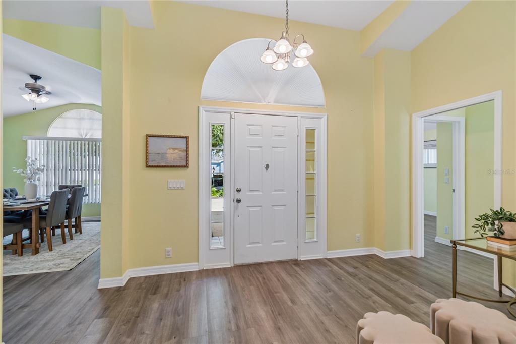 A bright entryway features light yellow walls, wood-look flooring, a white front door, and a chandelier — 12728 FLAMINGO PARKWAY, SPRING HILL, FL