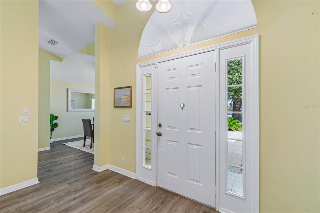 An entryway features a white front door with a sidelight, light yellow walls, and wood-look flooring — 12728 FLAMINGO PARKWAY, SPRING HILL, FL