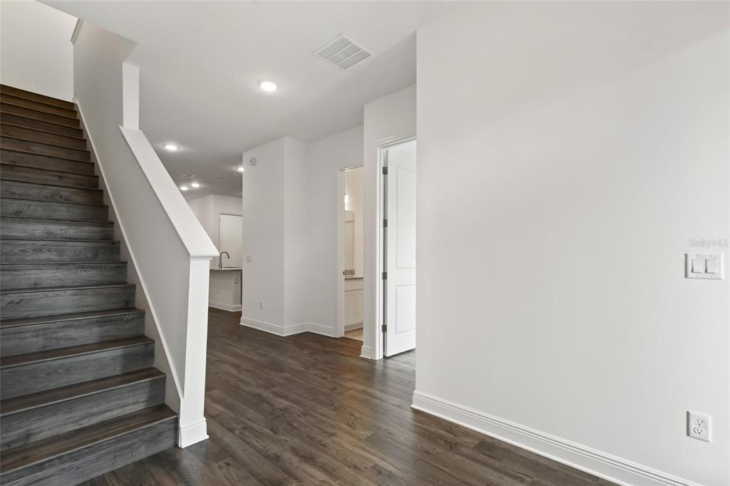A staircase with dark wood treads sits beside a hallway leading to a white interior — 2963 VOYAGER AVENUE, ST CLOUD, FL