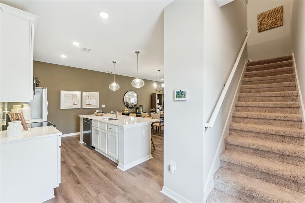 A kitchen with a white island and wood-look floors sits beside a carpeted staircase — 2302 RED PINE COURT, EUSTIS, FL