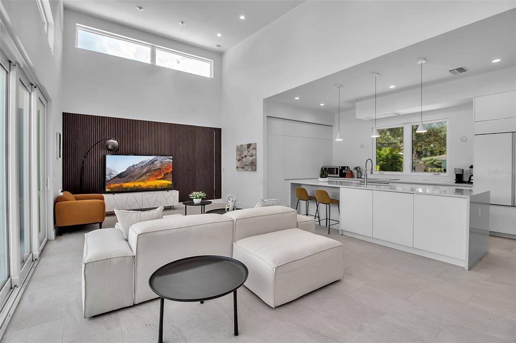 A modern open-concept living room and kitchen with white cabinetry, a sectional sofa, and wood-slatted wall — 2231 WOOD STREET, SARASOTA, FL