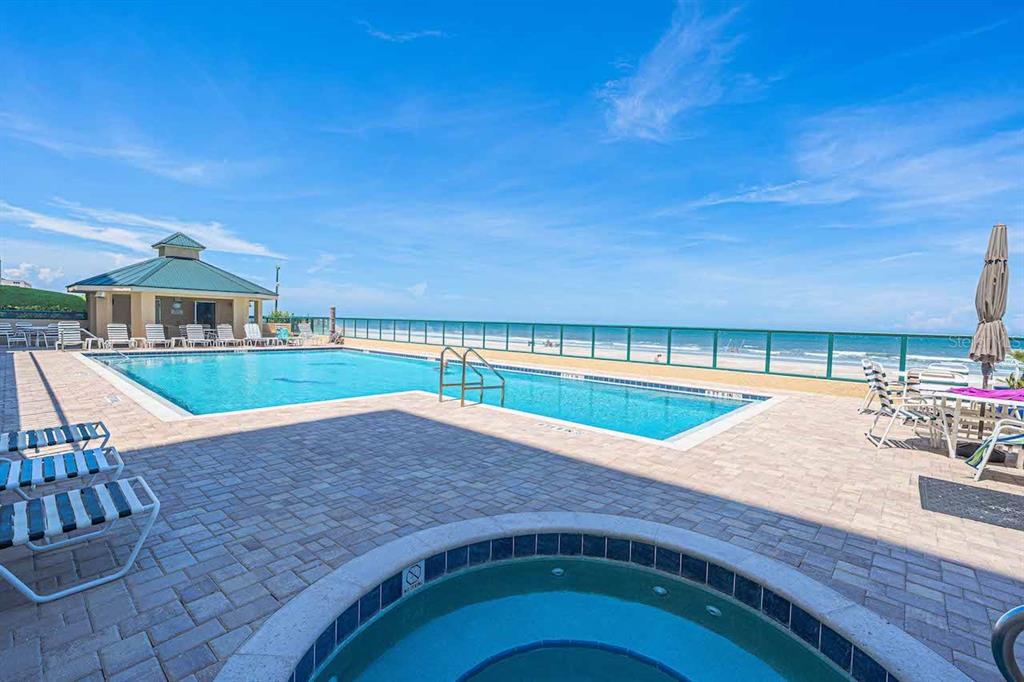 A swimming pool and hot tub overlook the ocean from a paved pool deck — 4575 S ATLANTIC AVENUE UNIT 6607, PONCE INLET, FL