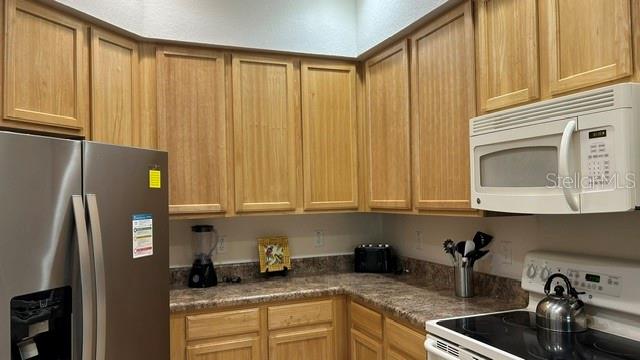A kitchen features light wood cabinets, a stainless steel refrigerator, and a white microwave — 3060 PIRATES RETREAT COURT UNIT 407, KISSIMMEE, FL