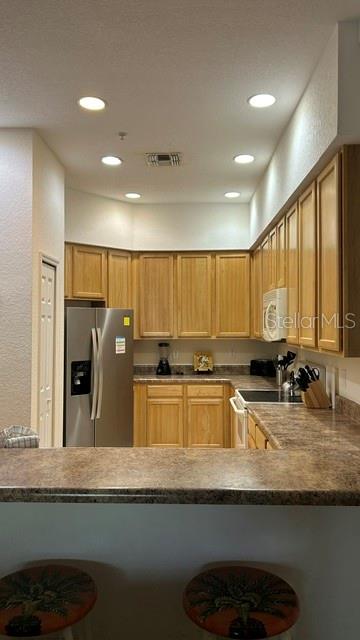 A kitchen features light wood cabinets, stainless steel appliances, and a breakfast bar with stools — 3060 PIRATES RETREAT COURT UNIT 407, KISSIMMEE, FL