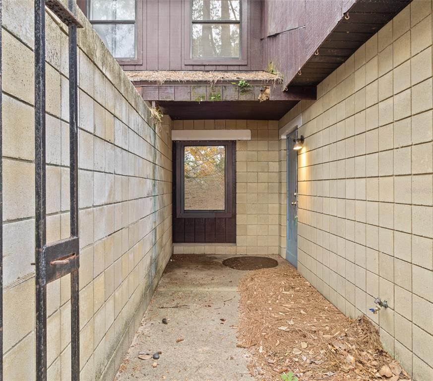 A concrete block entryway features a blue door, a small window, and pine needles — 4705 SW 69TH TERRACE, GAINESVILLE, FL