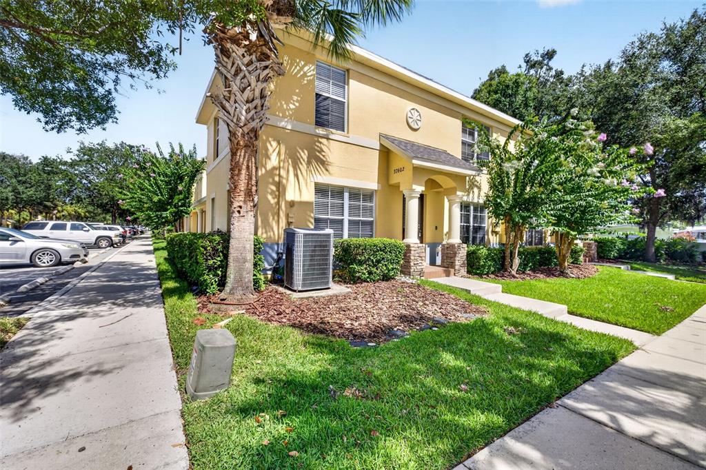 A two-story yellow stucco building features a covered entryway, palm tree, and air conditioning unit — 37602 AARALYN RD, ZEPHYRHILLS, FL