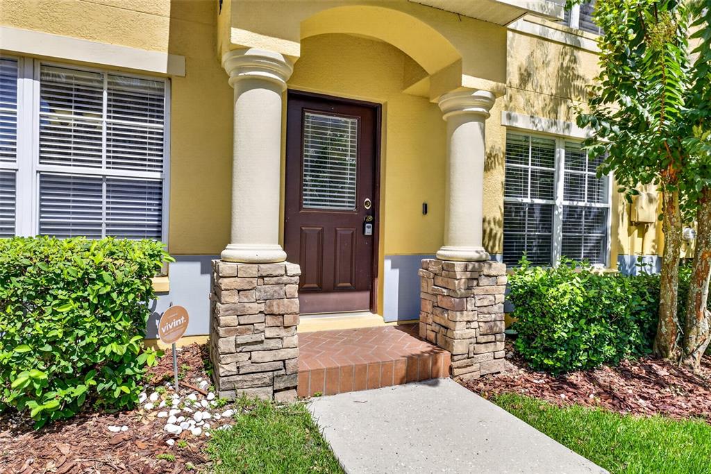 A front entrance with a brown door, stone-based columns, and a brick porch — 37602 AARALYN RD, ZEPHYRHILLS, FL
