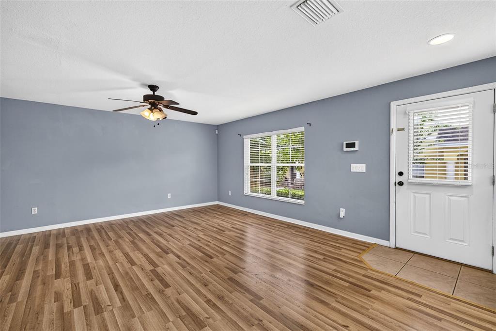 An empty living room features gray walls, wood-look flooring, a ceiling fan, and a front door — 37602 AARALYN RD, ZEPHYRHILLS, FL