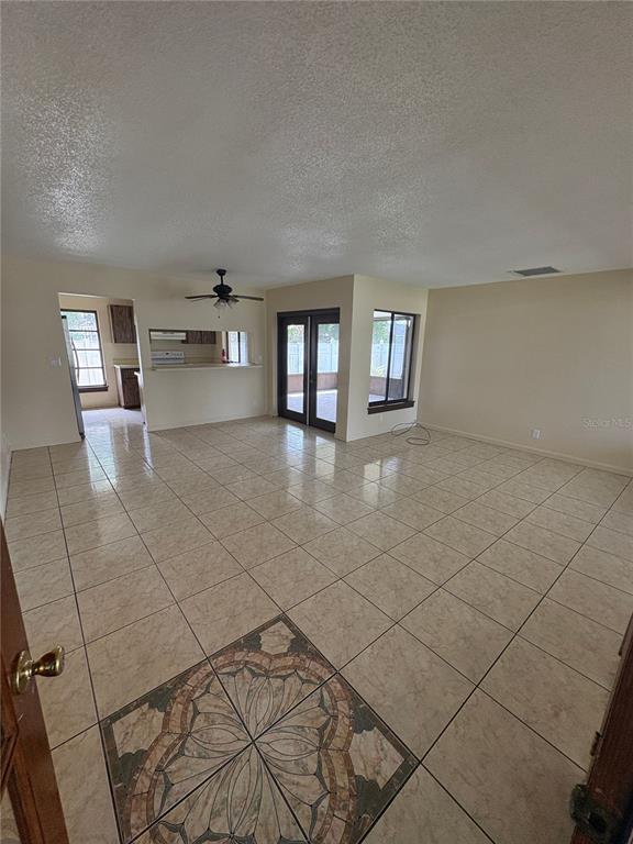 A spacious living area with light-colored tile flooring, a decorative inlay, and a kitchen pass-through — 11 TROPHY LANE, KISSIMMEE, FL