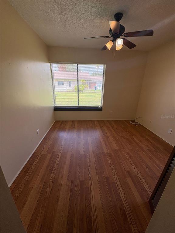 An empty bedroom features wood-look flooring, a ceiling fan, and a window overlooking a yard — 11 TROPHY LANE, KISSIMMEE, FL