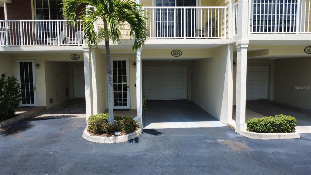A multi-unit building exterior features covered parking spaces, white railings, and a small palm tree — 3259 MANGROVE POINT DRIVE, RUSKIN, FL