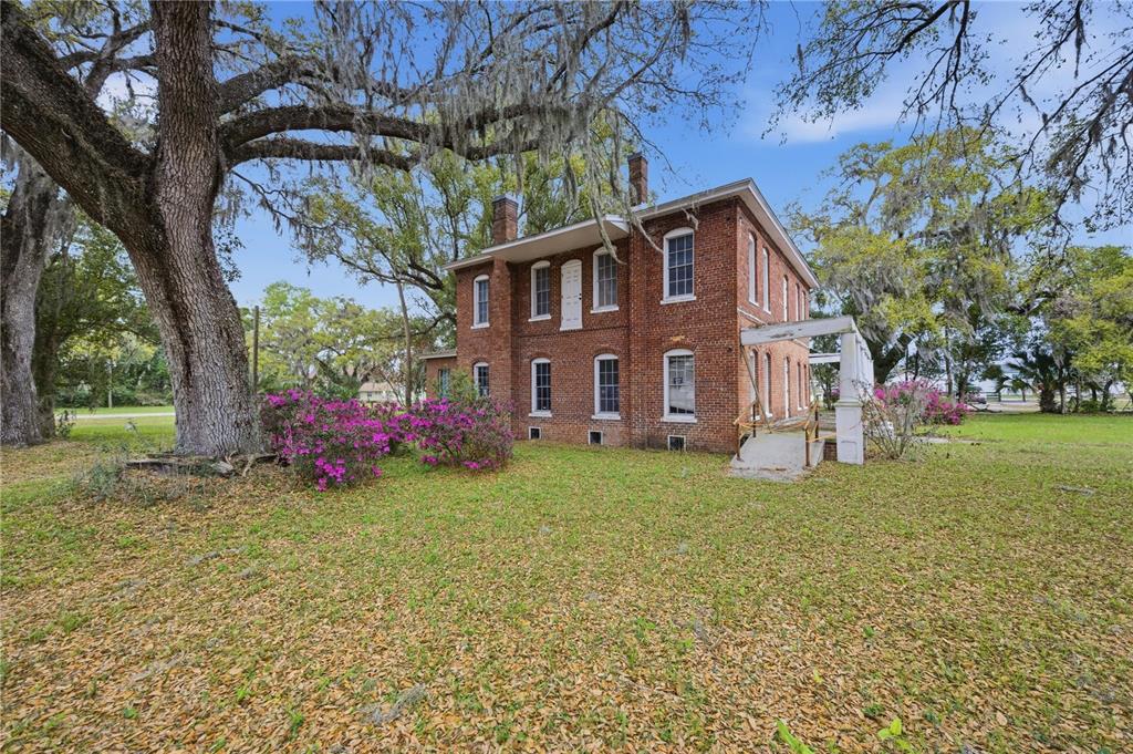 A two-story brick house sits on a grassy lawn under large, moss-draped oak trees — 120 N MAIN STREET, BUSHNELL, FL