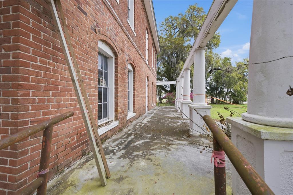 A brick building exterior features a long porch with white columns and metal railings — 120 N MAIN STREET, BUSHNELL, FL