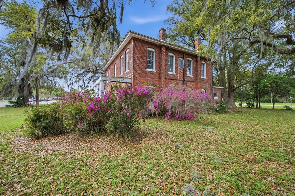 A two-story brick house with a white porch sits on a lawn with blooming azaleas — 120 N MAIN STREET, BUSHNELL, FL