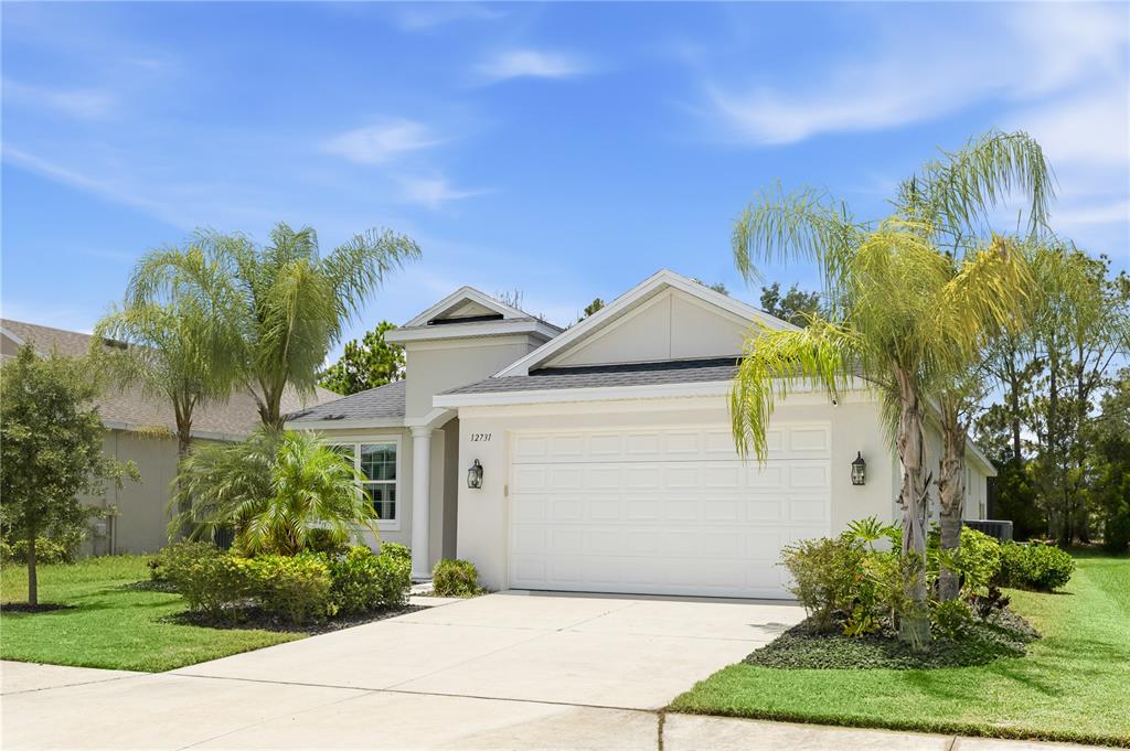 A single-story suburban house with a two-car garage, palm trees, and a concrete driveway — 12731 RAINWASHED LOOP, PARRISH, FL
