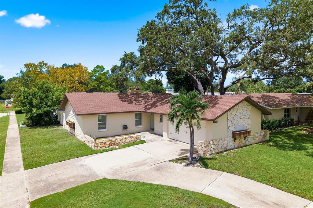 An exterior view of a single-story house with a stone facade, driveway, and large trees — 12620 115TH STREET, LARGO, FL