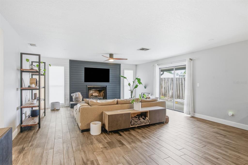 A living room features wood-look tile flooring, a dark shiplap fireplace wall, and a sectional sofa — 12620 115TH STREET, LARGO, FL