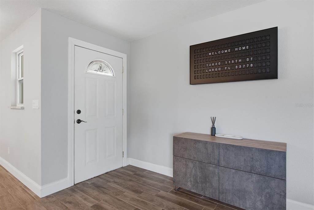 An entryway features a white door, wood-look tile flooring, a gray cabinet, and a letter board — 12620 115TH STREET, LARGO, FL