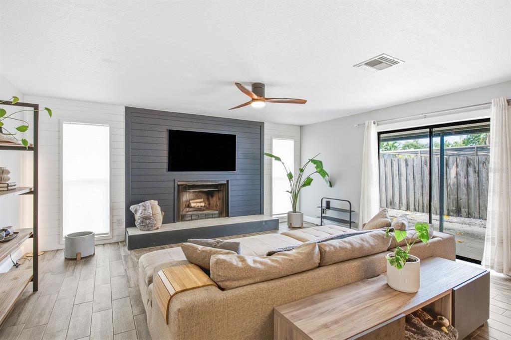 A living room features a dark shiplap fireplace wall, a sectional sofa, and sliding glass doors — 12620 115TH STREET, LARGO, FL