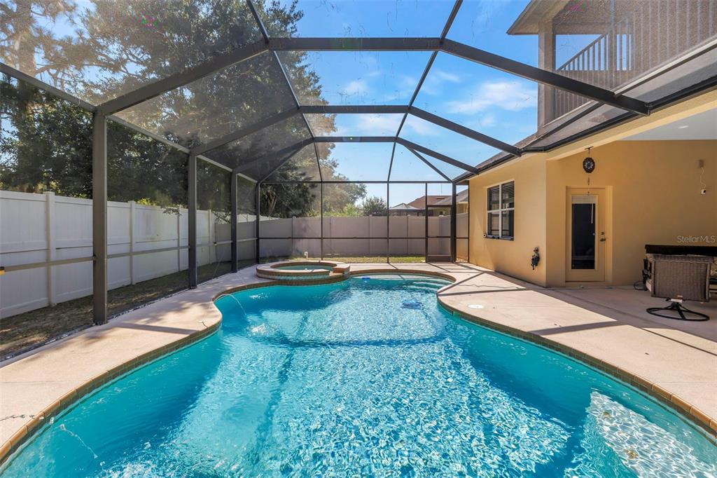 A backyard swimming pool and hot tub enclosed by a screened lanai behind a house — 27405 SORA BOULEVARD, WESLEY CHAPEL, FL