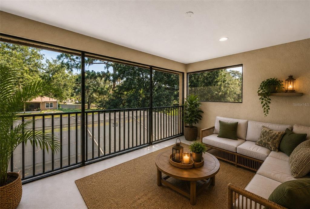 A modern living room features a large sectional, a circular coffee table, and pool views — 27405 SORA BOULEVARD, WESLEY CHAPEL, FL