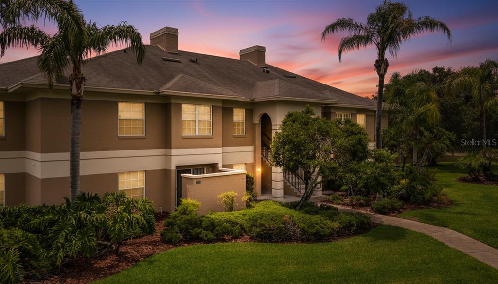 A two-story apartment building with beige stucco siding, a shingled roof, and landscaped grounds — 704 EAGLE POND DRIVE UNIT 704, WINTER HAVEN, FL