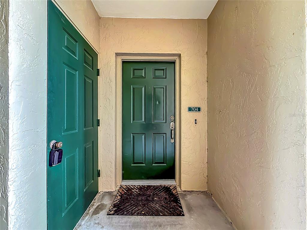 A green front door with a "704" sign sits in a beige entryway — 704 EAGLE POND DRIVE UNIT 704, WINTER HAVEN, FL