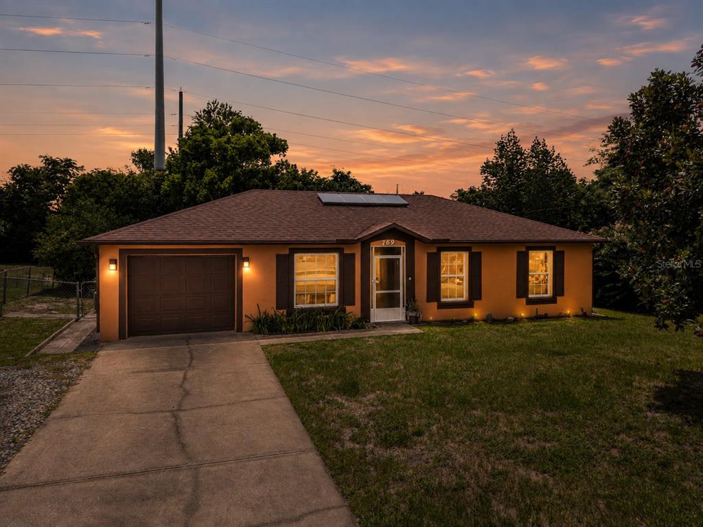 A single-story house with an orange stucco exterior, a brown roof, and a concrete driveway — 769 TRUMBULL STREET, DELTONA, FL