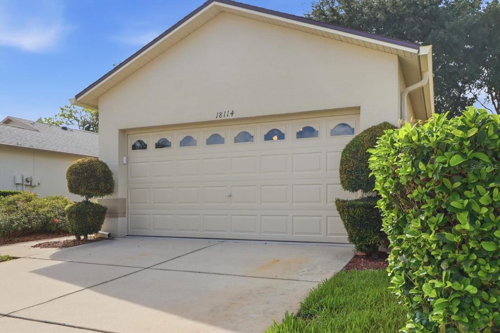 A beige house exterior features a two-car garage with arched windows and manicured landscaping — 18114 BRELAND DRIVE, HUDSON, FL
