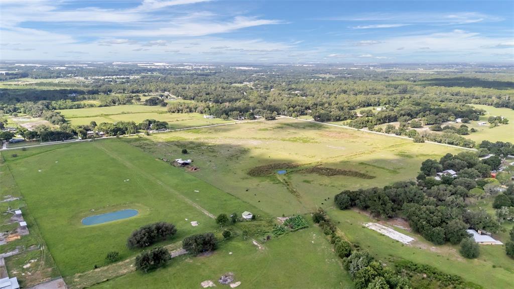 An aerial view shows a large, grassy pasture with a small pond and scattered trees — 4025 W BELLA VISTA STREET, LAKELAND, FL