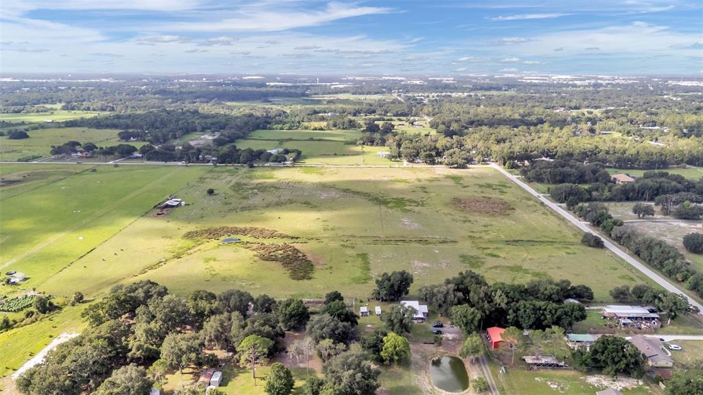 An aerial view shows a large, flat pasture with scattered trees, a pond, and buildings — 4025 W BELLA VISTA STREET, LAKELAND, FL