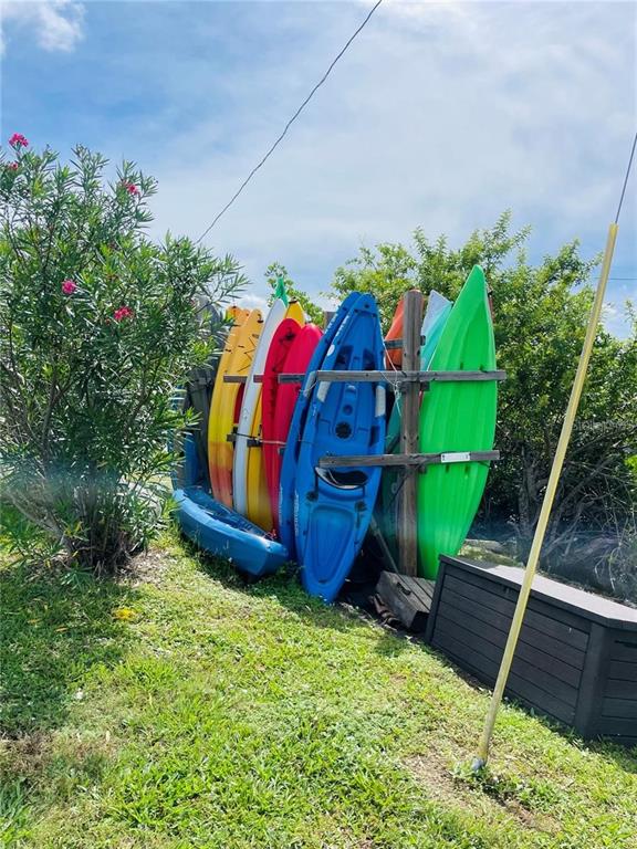 A rack holds several colorful kayaks upright in a grassy outdoor area near a bush — 160 NEW YORK STREET, PALMETTO, FL