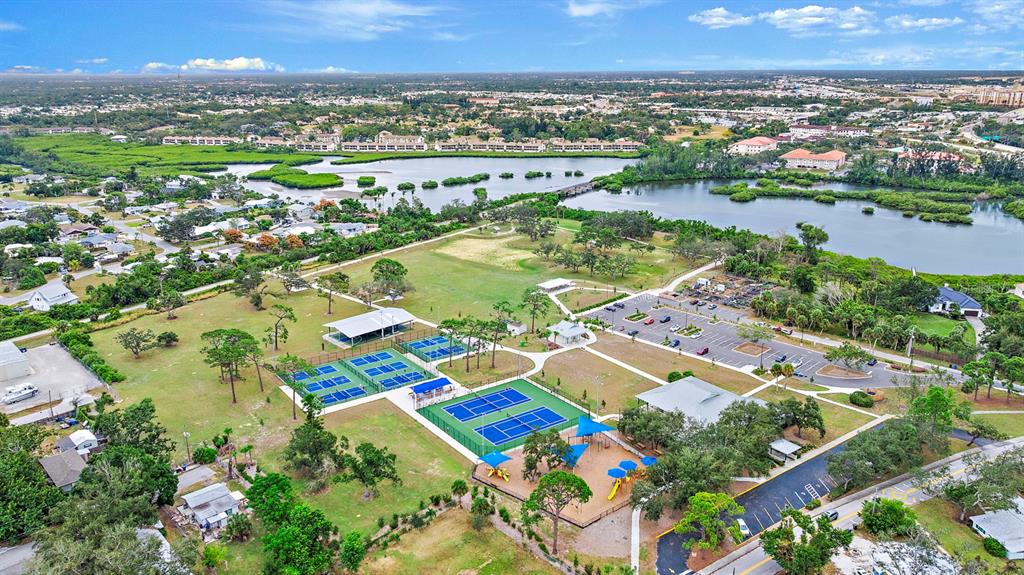 An aerial view shows tennis courts, a playground, a parking lot, and a nearby lake — COLONIA LANE, NOKOMIS, FL
