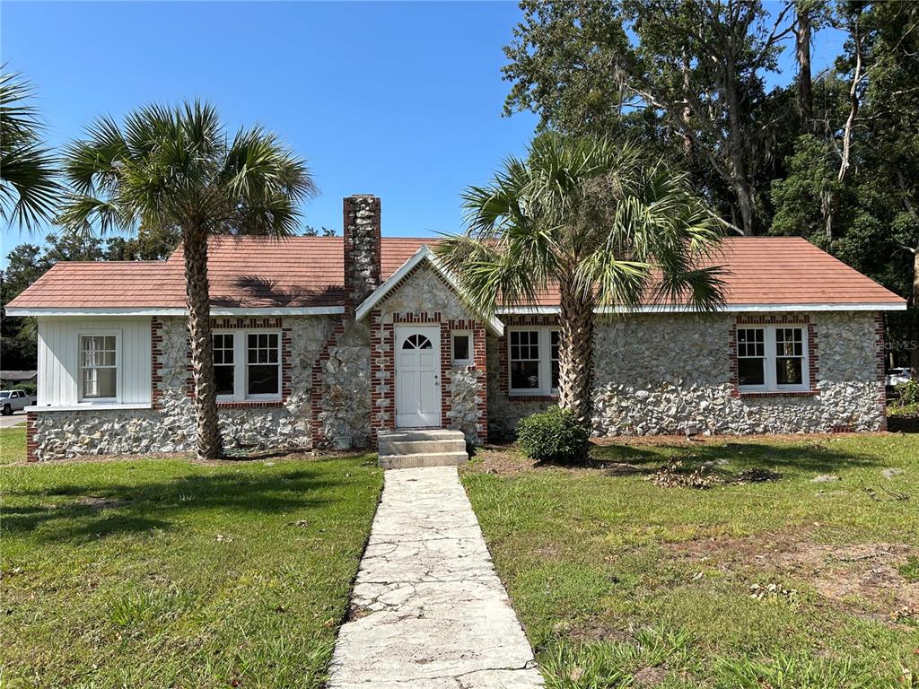 A single-story stone house with a red roof, a central chimney, and two palm trees — 1008 NW 13TH STREET, GAINESVILLE, FL