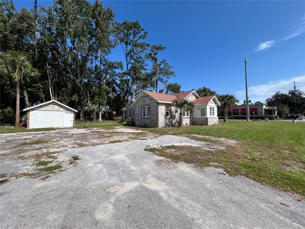 A stone-clad house with a brown roof sits on a lot with a paved area — 1008 NW 13TH STREET, GAINESVILLE, FL