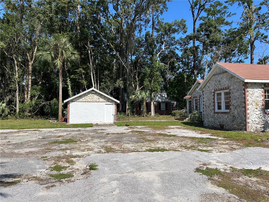 A stone-faced house with a detached garage sits on a large, weathered asphalt lot — 1008 NW 13TH STREET, GAINESVILLE, FL