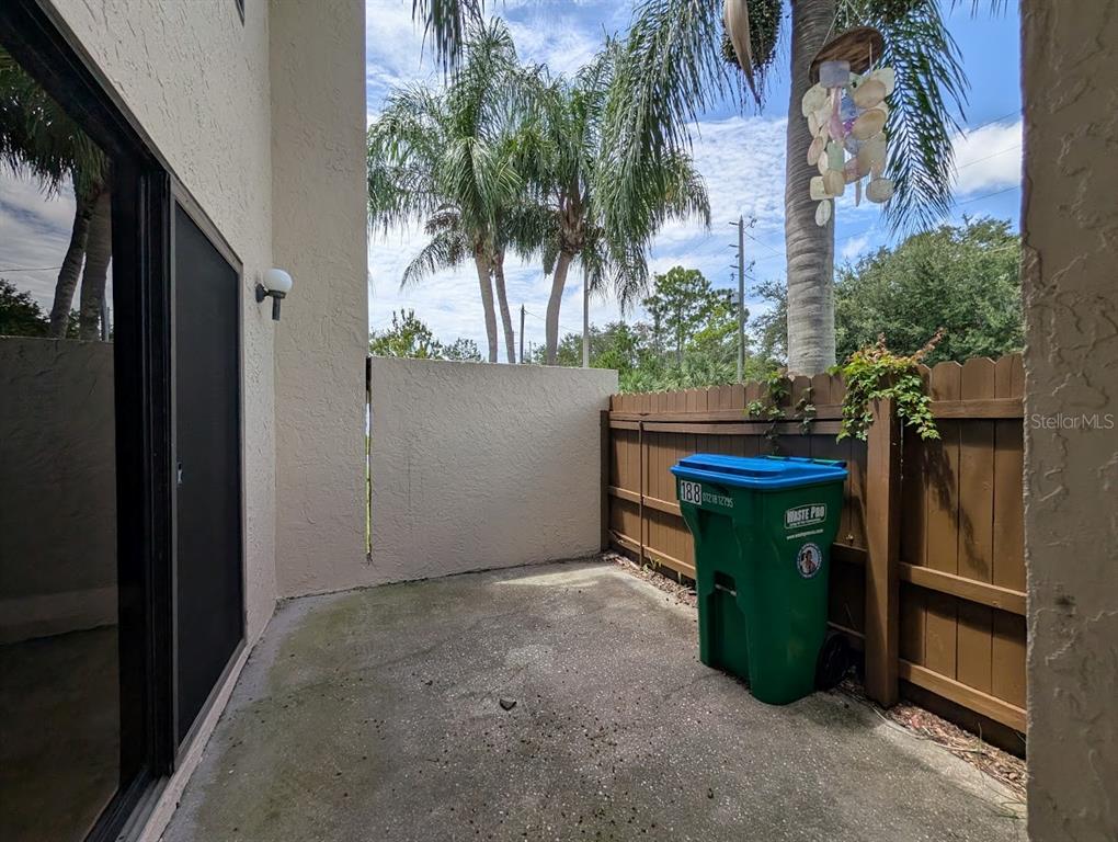 A concrete patio features a green waste bin, a wooden fence, and palm trees overhead — 9209 SEMINOLE BOULEVARD UNIT 188, SEMINOLE, FL