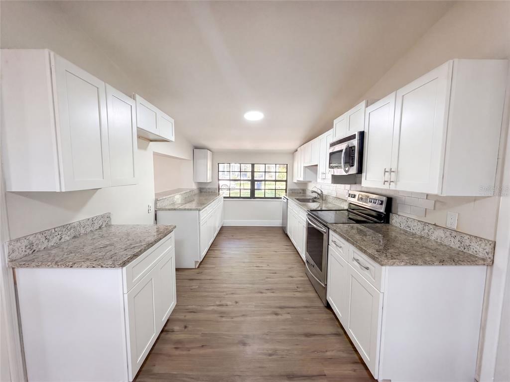 A galley kitchen features white cabinets, granite countertops, stainless steel appliances, and wood-look flooring — 7405 S DESOTO STREET, TAMPA, FL