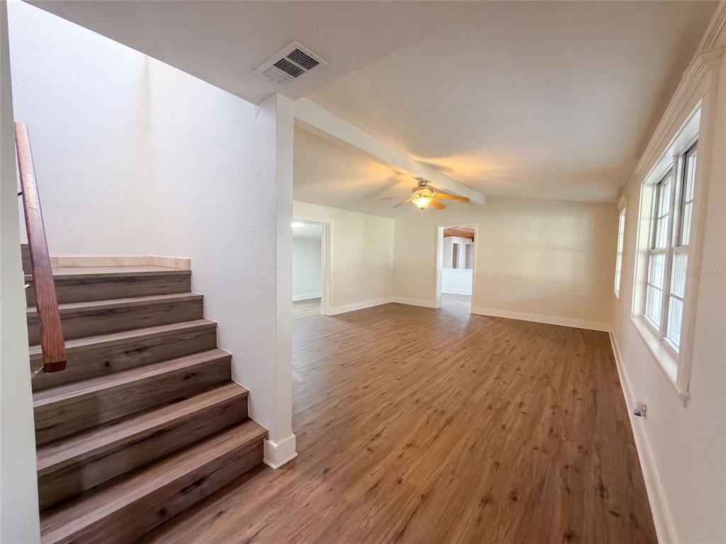 A room with wood-look flooring, a staircase with a wooden handrail, and a ceiling fan — 7405 S DESOTO STREET, TAMPA, FL