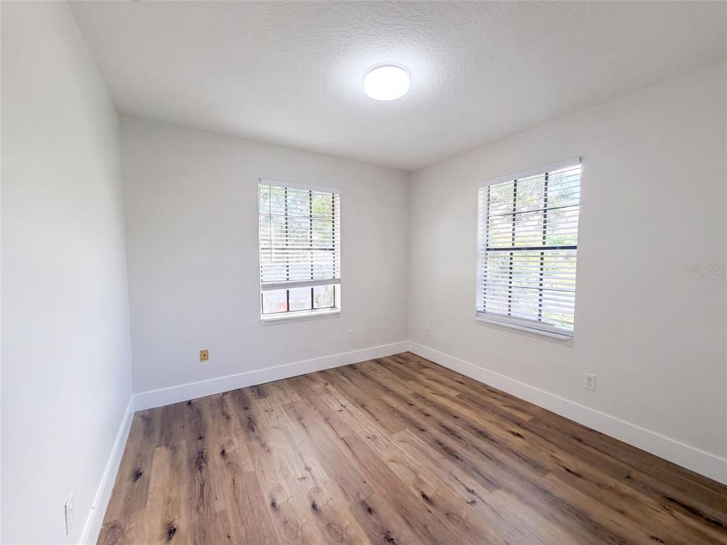 An empty bedroom features white walls, wood-look flooring, and two windows with white blinds — 7405 S DESOTO STREET, TAMPA, FL