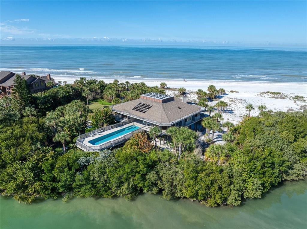 An aerial view of a beachfront house with a rectangular pool and solar panels — 1198 MANDALAY POINT, CLEARWATER, FL