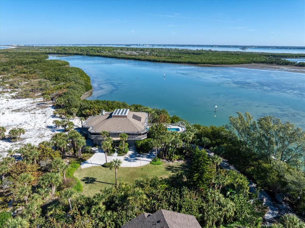 An aerial view shows a house with a pool surrounded by trees and water — 1198 MANDALAY POINT, CLEARWATER, FL