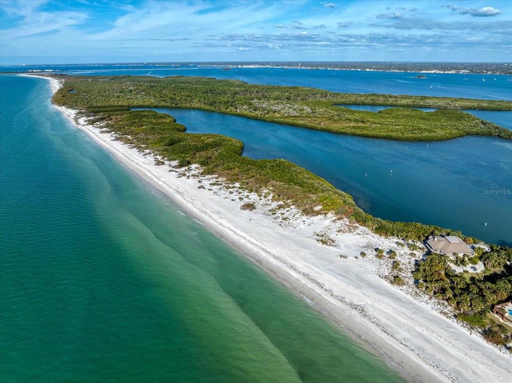 An aerial view shows a sandy beach bordering a lush island with a large house — 1198 MANDALAY POINT, CLEARWATER, FL
